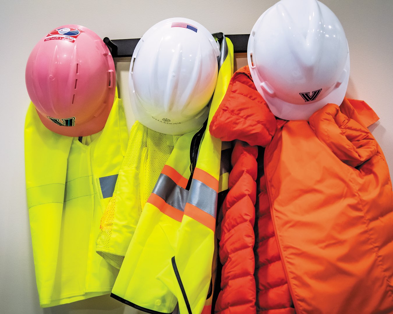 A coat rack in senior project manager Marilou Smith’s office with three Villanova hard hats and yellow and orange safety gear