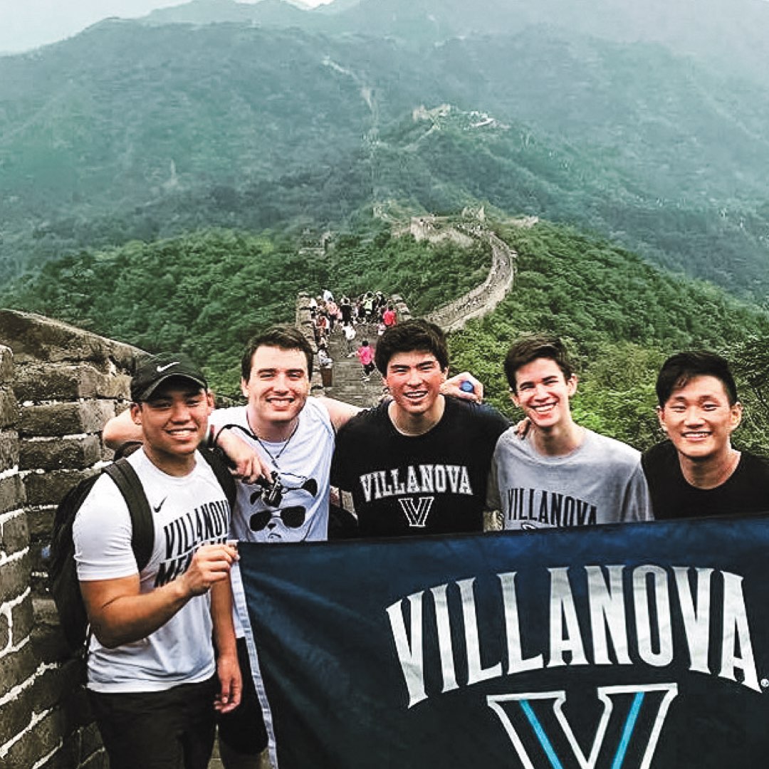 Five male Villanova students in Villanova T-shirts holding a Villanova banner in front of the Great Wall of China