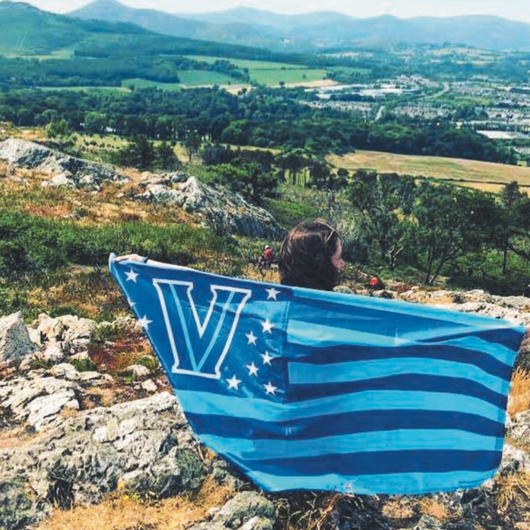 A female Villanova student holding an American flag Villanova banner in front of the green hills of Bray, Co. Wicklow in Ireland 