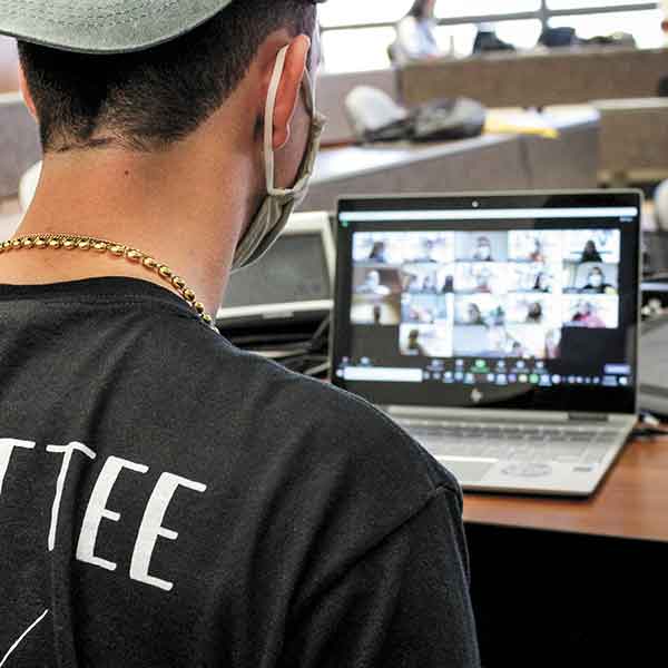 the back of a masked student looking at a laptop screen with a video meeting