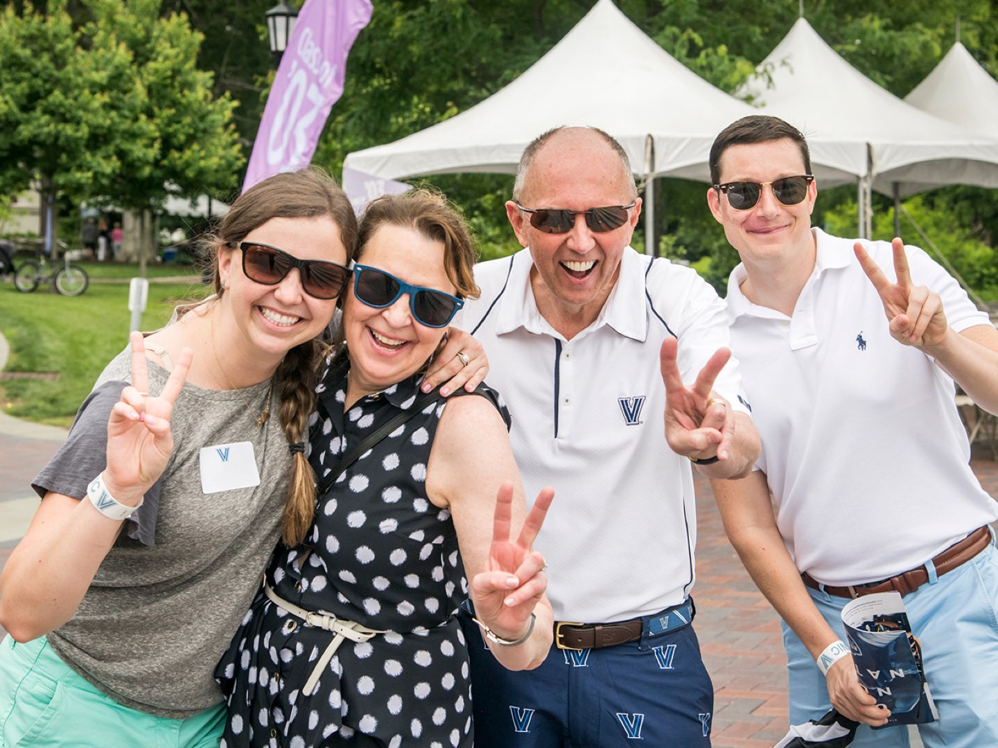Four Villanova alumni holding up their fingers in V-shapes.
