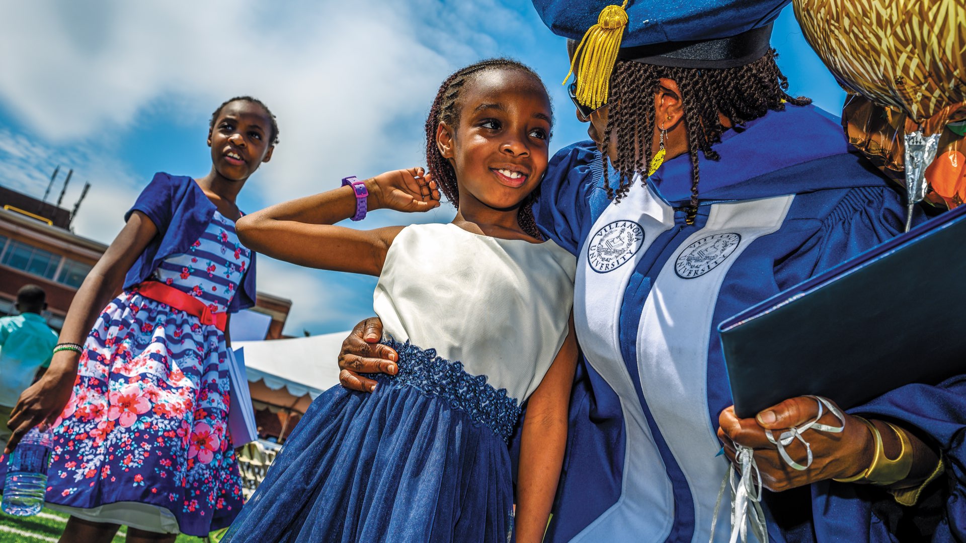 A mother in her graduation regalia with diploma in hand hugs her young daughter