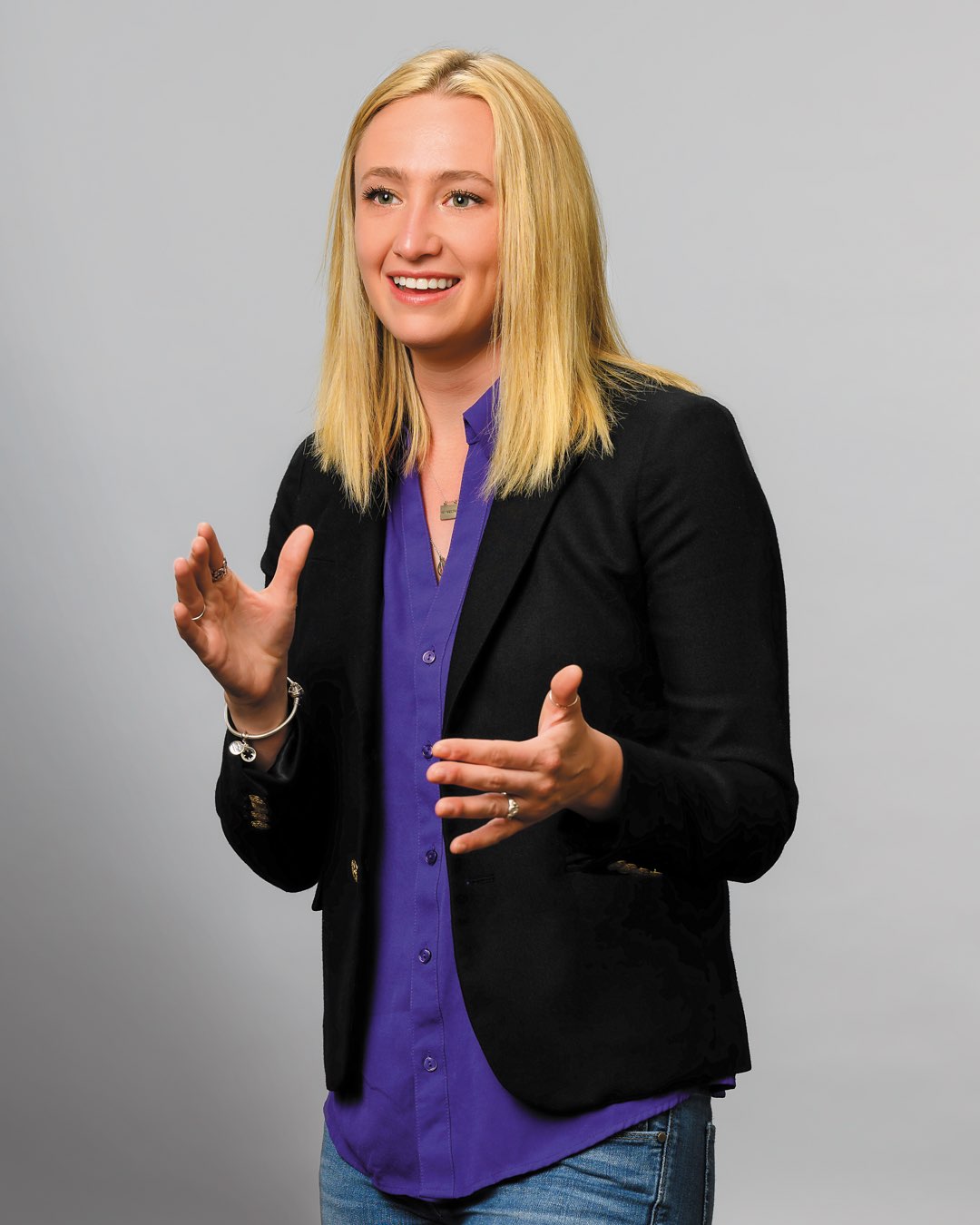 Talking with her hands, recent CLAS graduate MK Smith is wearing a blazer with jeans and a purple shirt