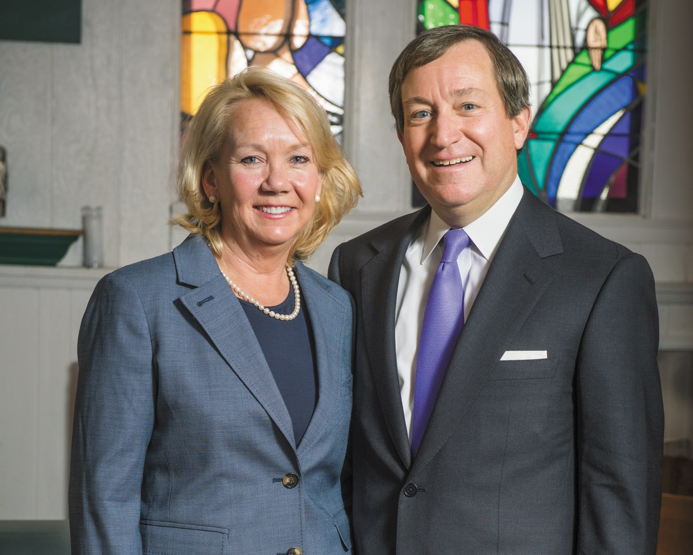 Polly and Terry O’Toole smiling in front of stained glass windows in the chapel