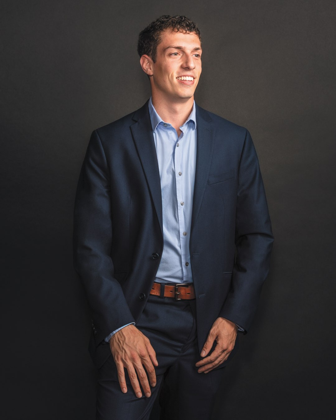 Recent graduate Alex Alberti standing in a navy suit and blue dress shirt