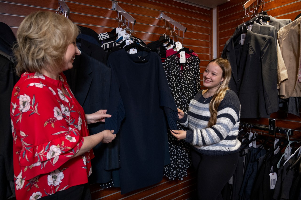 Student standing in the wardrobe looking at a dress with a career center staff member.