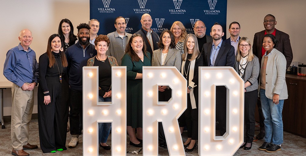 Villanova HRD faculty standing together at a retreat image of faculty standing behind large HRD display