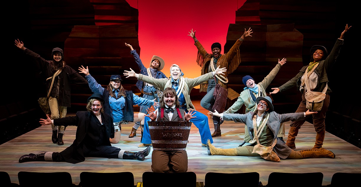 Performers smiling and posing on stage with arms spread wide Performers smiling and posing on stage with arms spread wide