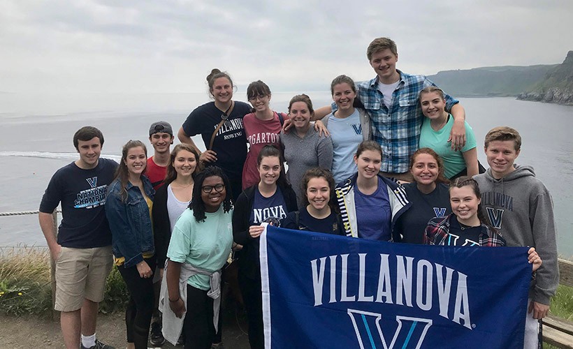 Villanova students with flag. A group of students stand on the cliffs of Ireland with a Villanova flag.