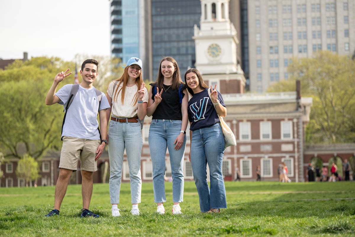 Four students throwing up a peace sign and smiling