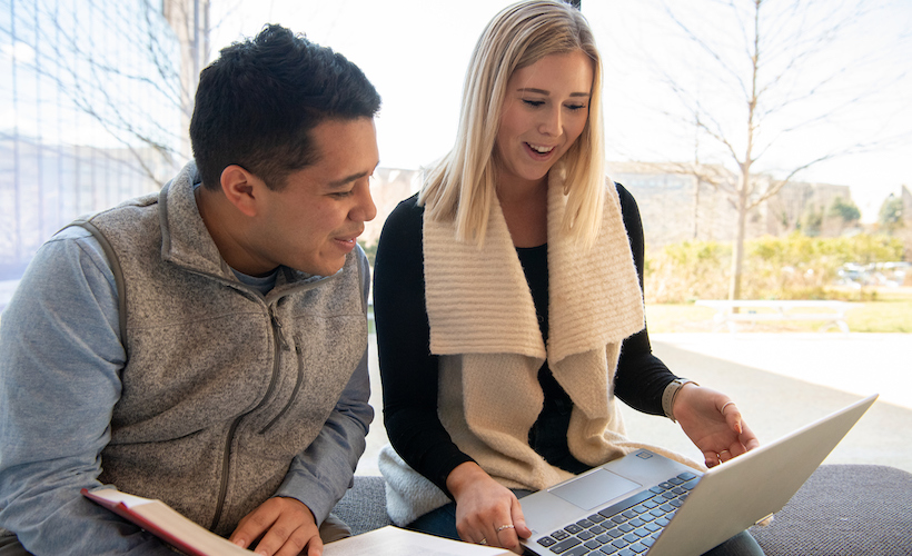 Two students work together and look at a shared computer screen.