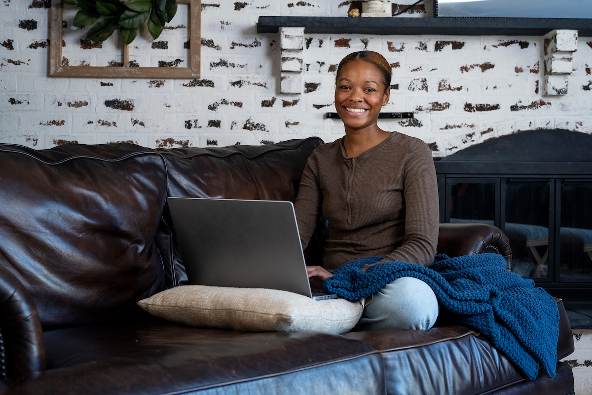 woman sitting on a sofa with a laptop looking at the camera and smiling