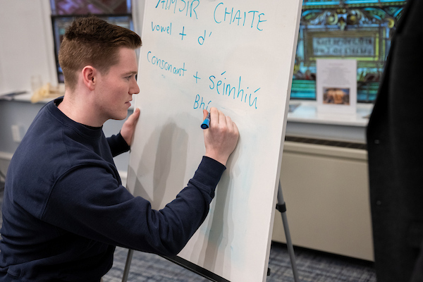 Male student writing Gaelic on a whiteboard