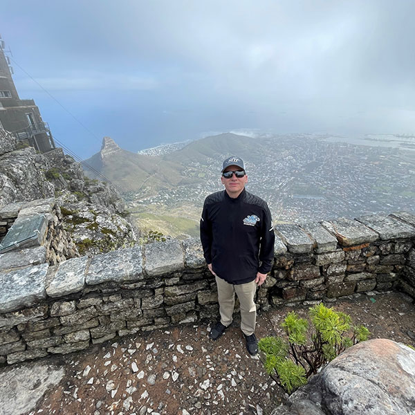 a man stands in front of a stone wall under a cloudy sky