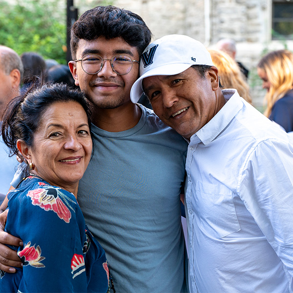 A male student poses with his arms around his mom and dad at New Student Orientation.