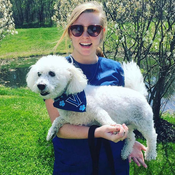 a fluffly white dog wearing a Villanova bandanna held by a young woman 
